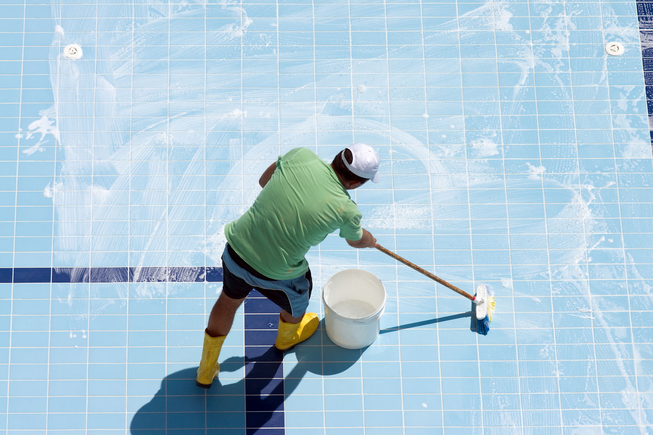 Man cleaning the tiled floor of swimming-pool.